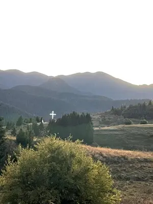 a white cross in the middle of a field with mountains at Marina apartment in Stoykite