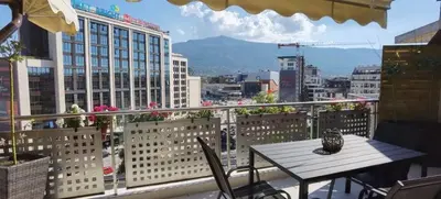 a table and chairs on a balcony with a view of a city at Cozy Apartment with Mountain View & Parking in Sofia