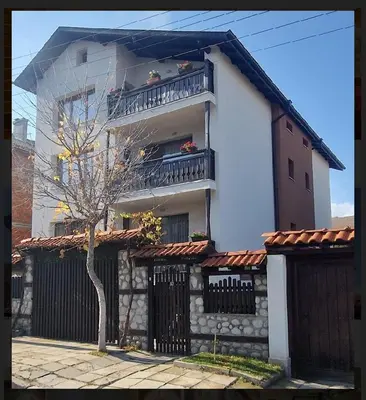 a white building with a balcony and a tree at Къща за гости Карасански in Bansko