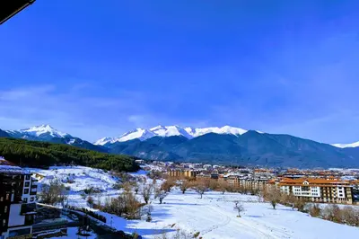 a city with snow covered mountains in the background at Stylish 2BD Apartment with Panoramic Mountain View by Flat Mаnager in Bansko