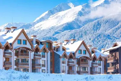 a hotel with snow covered mountains in the background at Stylish Cozy Studio with fireplace in Bansko