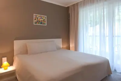a bedroom with a white bed and a window at Парк хотел Кюстендил in Kyustendil