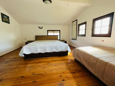 a bedroom with two beds and wooden floors and windows at Къща за гости Под Манастира in Skrino