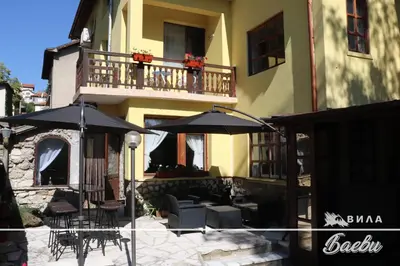 a patio with chairs and umbrellas in front of a building at ВИЛА БАЕВИ in Velingrad