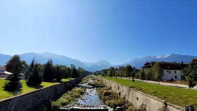 a river flows along a stone wall with mountains in the background at Cozy studio with balcony and incl SPA in 4-star hotel Saint Ivan Rilski , Bansko in Bansko