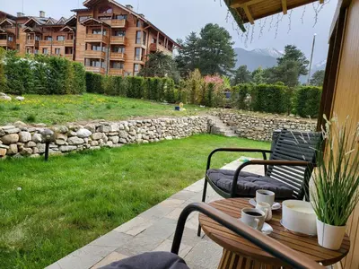 a patio with two chairs and a table and a stone wall at Boutique Holiday Pirin Golf in Razlog